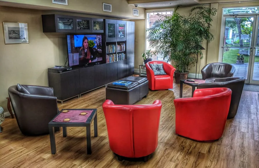 The Inglewood House community lounge, with red and leather armchairs, a television and large sunny windows