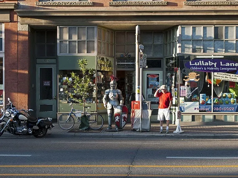 Shopfronts on 9th Avenue, with a suit of armour on the sidewalk and bicycles parked outside